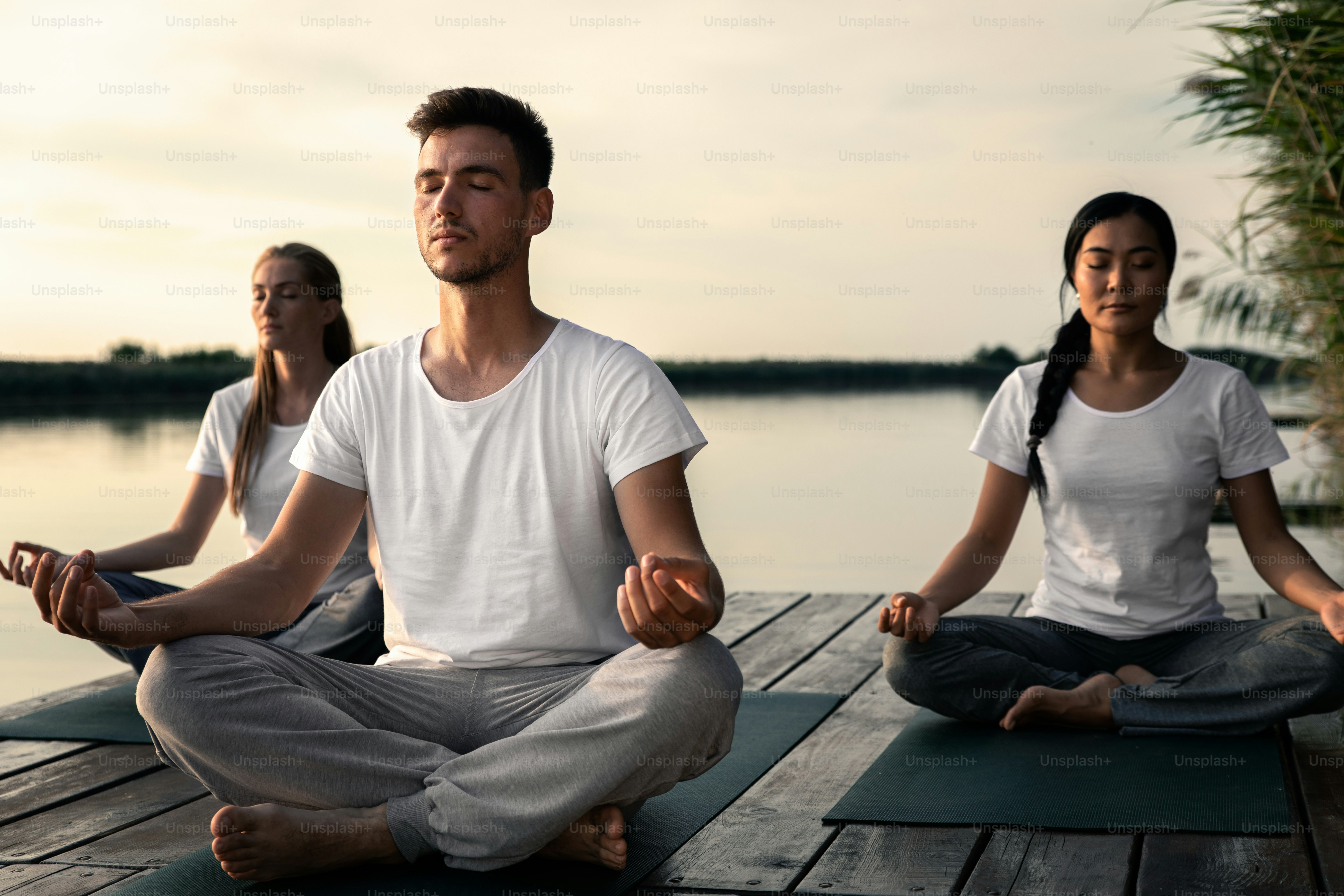 Group of people doing yoga exercises by the lake at sunset.