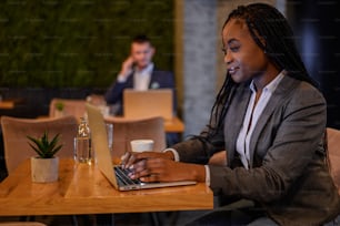 젊은 아름다운 아프리카계 미국인 사업가가 카페에서 커피를 마시면서 노트북으로 작업