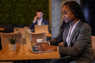 Young beautiful african american businesswoman working on her laptop while drinking coffee in a cafe