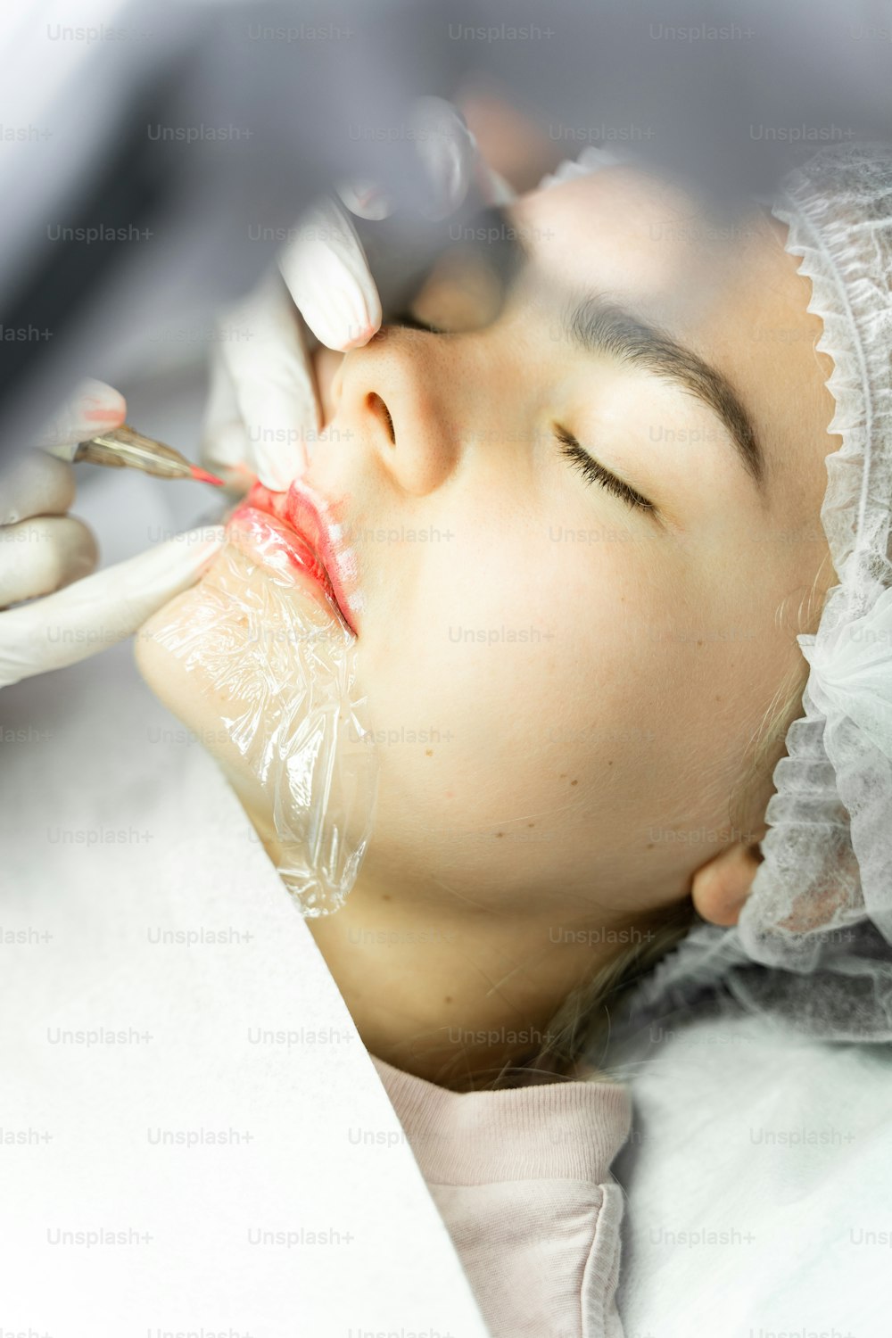 Giovane donna durante la procedura di trucco permanente professionale - arrossamento delle labbra