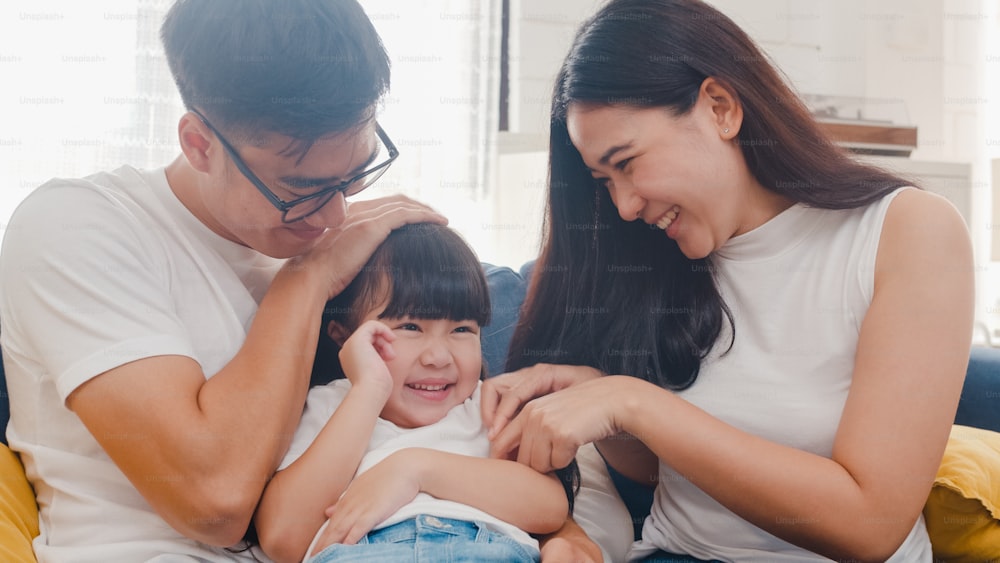 Happy cheerful Asian family dad, mom and daughter having fun cuddling playing on sofa while birthday at house.