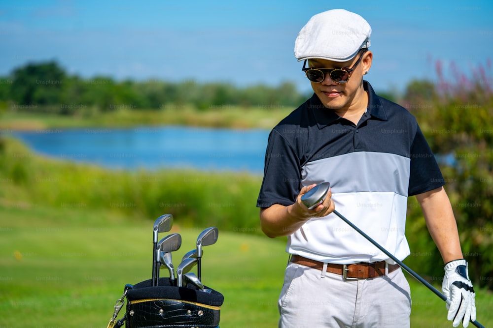 Ritratto di uomo asiatico sorridente che tiene la mazza da golf in piedi sul fairway del campo da golf in una giornata di sole. Il golfista maschio sano si gode lo stile di vita all'aria aperta, l'attività, lo sport, il golf al country club durante le vacanze estive