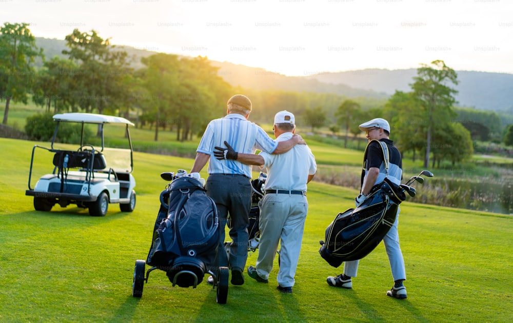 Group of Asian people businessman and senior CEO enjoy outdoor sport  golfing together at country club. Healthy men golfer holding golf bag walking on fairway with talking together at summer sunset