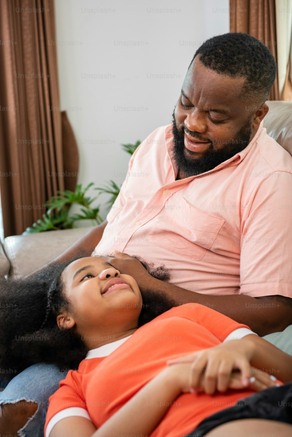 Happy African family spending time together at home. Little daughter lying on father lap on sofa in living room with talking together. Smiling dad and child girl kid resting and relaxing together.