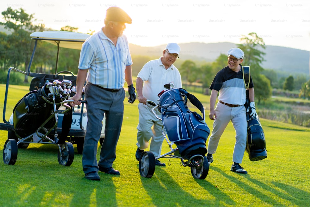 アジア人のグループ、ビジネスマン、シニアCEOは、カントリークラブで一緒にアウトドアスポーツゴルフを楽しんでいます。夏の夕暮れ時にフェアウェイを歩きながらゴルフバッグを持つ健康な男性ゴルファー