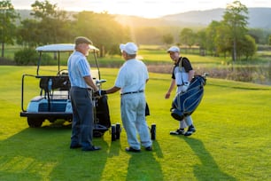 Group of Asian people businessman and senior CEO enjoy outdoor sport  golfing together at country club. Healthy men golfer holding golf bag walking on fairway with talking together at summer sunset