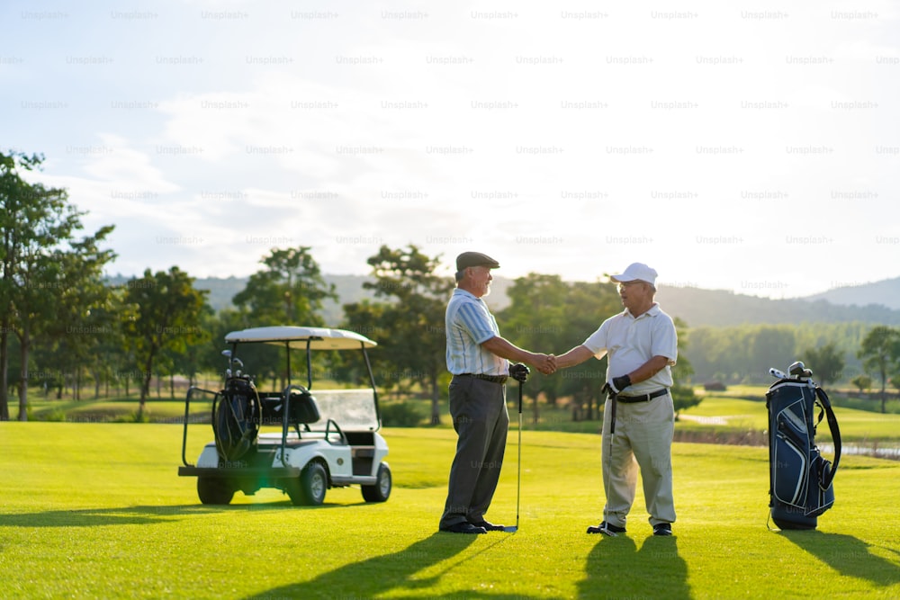 Asian people businessman senior CEO shaking hand after finish talking business project and golfing together at golf course. Elderly male friends golfer enjoy outdoor sport golfing together at country club.