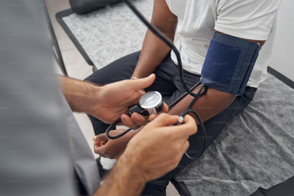 Beschnittenes Foto eines männlichen Patienten, der während der Blutdruckmessung auf der Couch sitzt