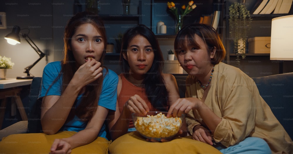 Group of attractive Asia lady girl freaking out fear and terrified moment eat popcorn watch horror online movie on couch in living room at home in night.