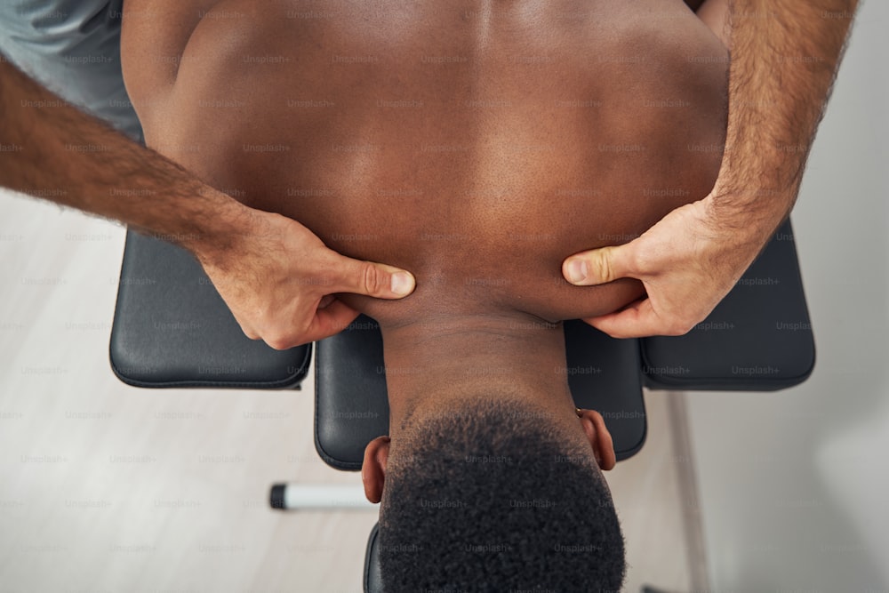 Foto cortada de mãos de massoterapeuta profissional caucasiano massageando o pescoço de pacientes afro-americanos