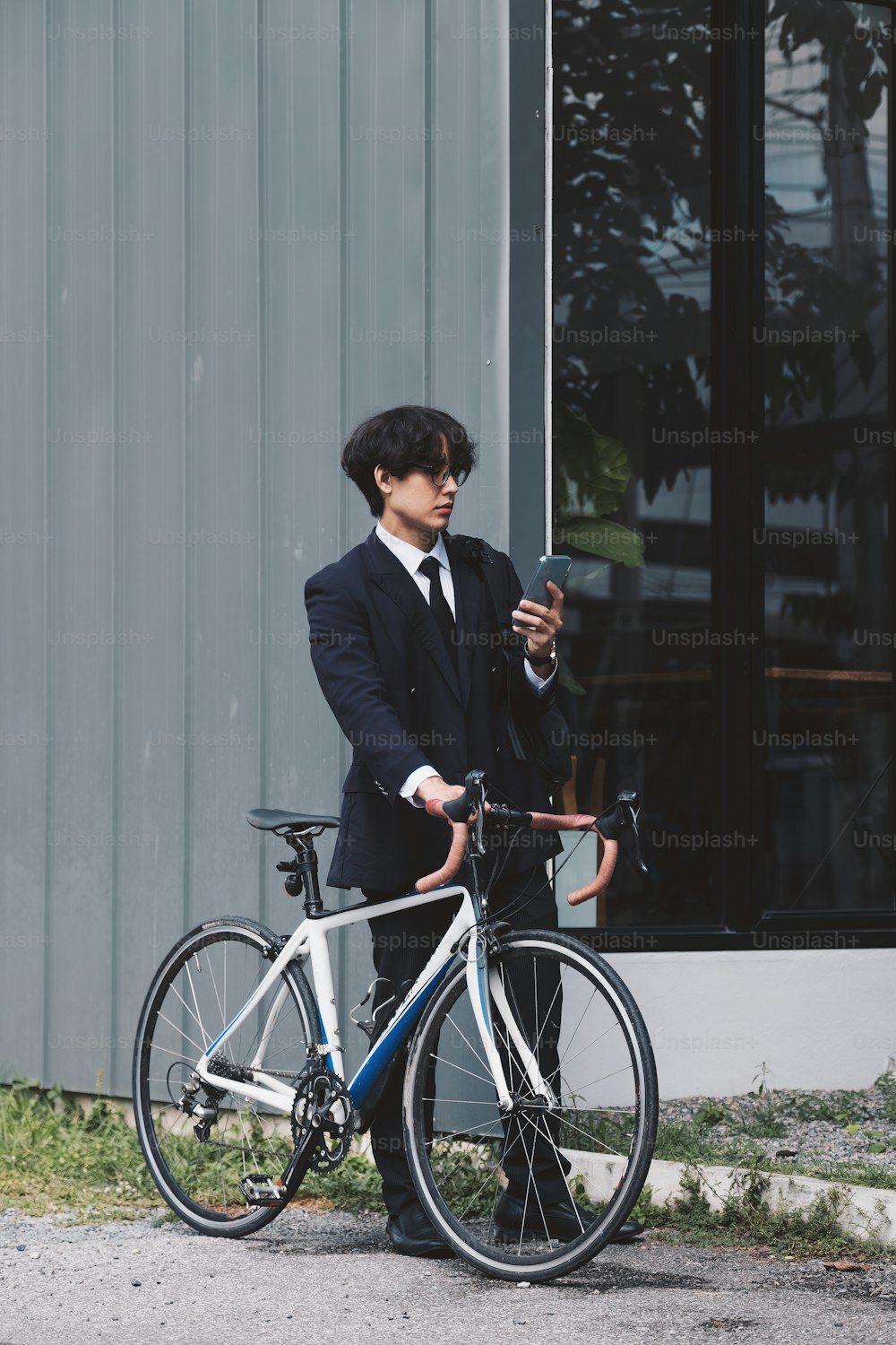 Retrato de un hombre de negocios asiático empujando su bicicleta por la mañana con un teléfono móvil.