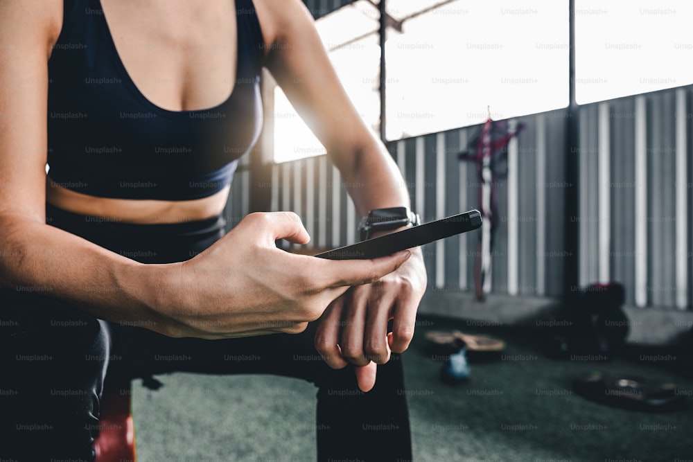 Sport woman resting after workout during use smartwatch connect smartphone workout app. Indoors gym background. Health sport concept