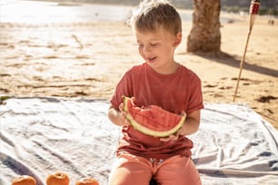 Petit garçon heureux sur la plage de pique-souriant, mangeant de la pastèque, se détendant. Journée ensoleillée d’été.