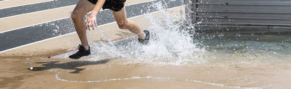 Un liceale sta sguazzando nell'acqua mentre esce dal pozzo d'acqua siepi durante una gara su pista.