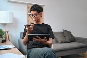 Smiling young asian man talking on mobile phone and using digital tablet at home.