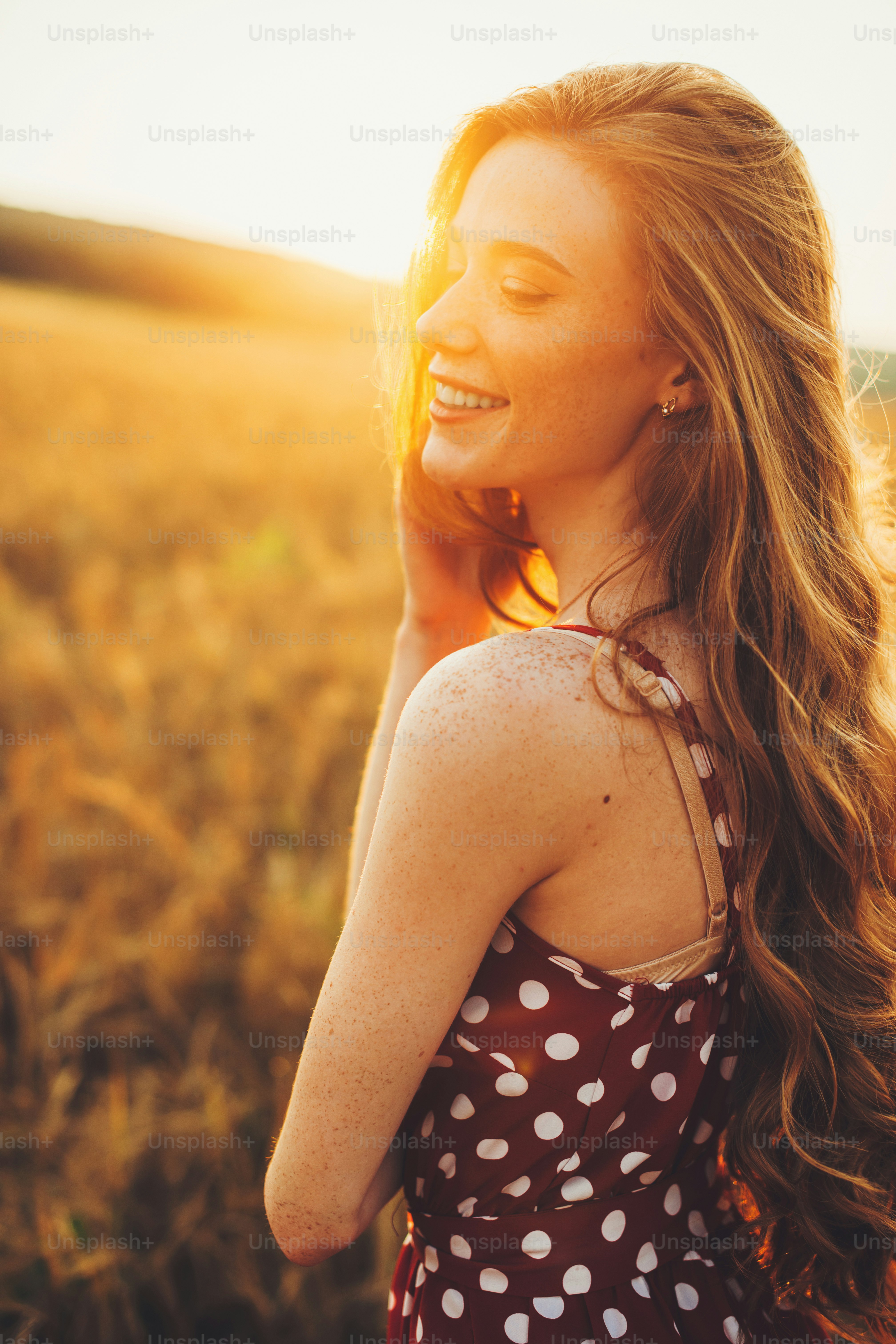 View from the side of a young woman smiling in the wheat field. Freckled face and shoulders. Sunset in the wheat field