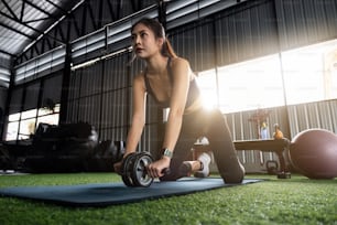 Close up of asian sports woman is doing ab roller exercise while working out on fitness center background. Concept woman health care