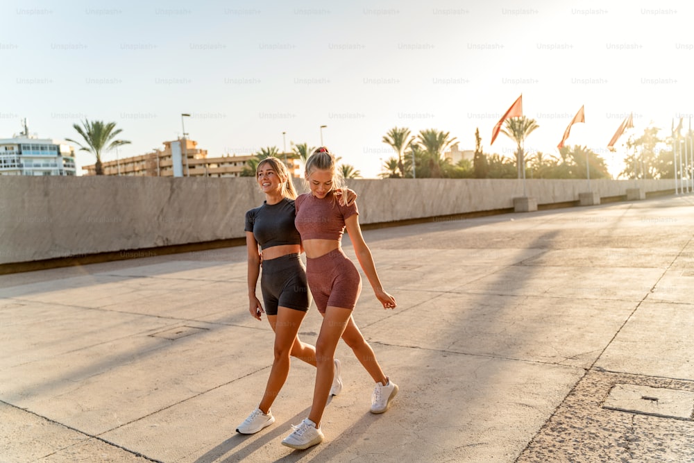 Tired beautiful fit blonde women taking a break, happy after outdoor workout. Two friends training together. Sport. Hobby. Girls with ideal slim bodies.