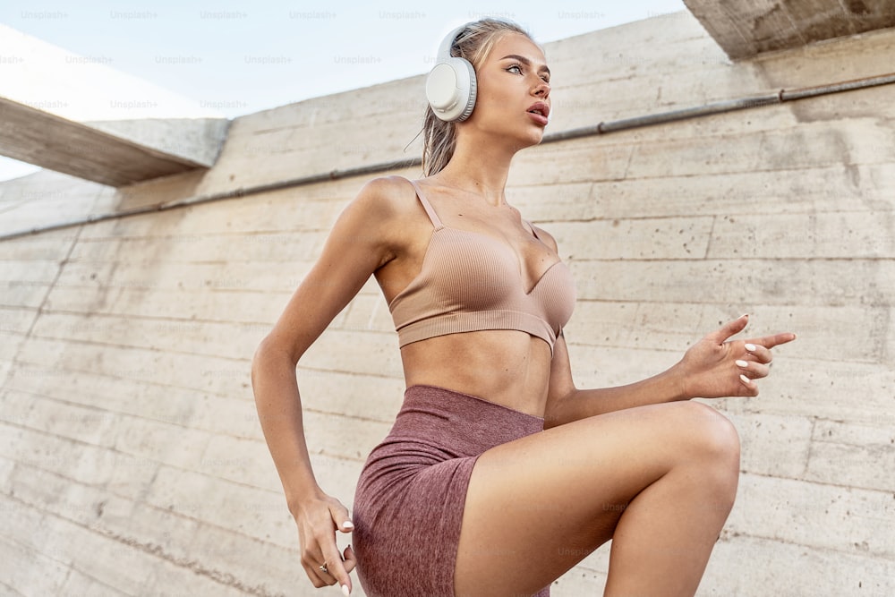 Young beautiful fit caucasian woman exercising outdoors. Attractive girl with headphones running. Healthy sporty lifestyle concept. Morning routine.