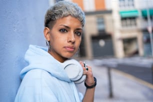 Joven hermosa mujer con corte de pelo corto posando con auriculares blancos, mirando a la cámara. Emociones de personas reales. Afición. Dj. Concepto de estilo de vida. Paseo por la ciudad.