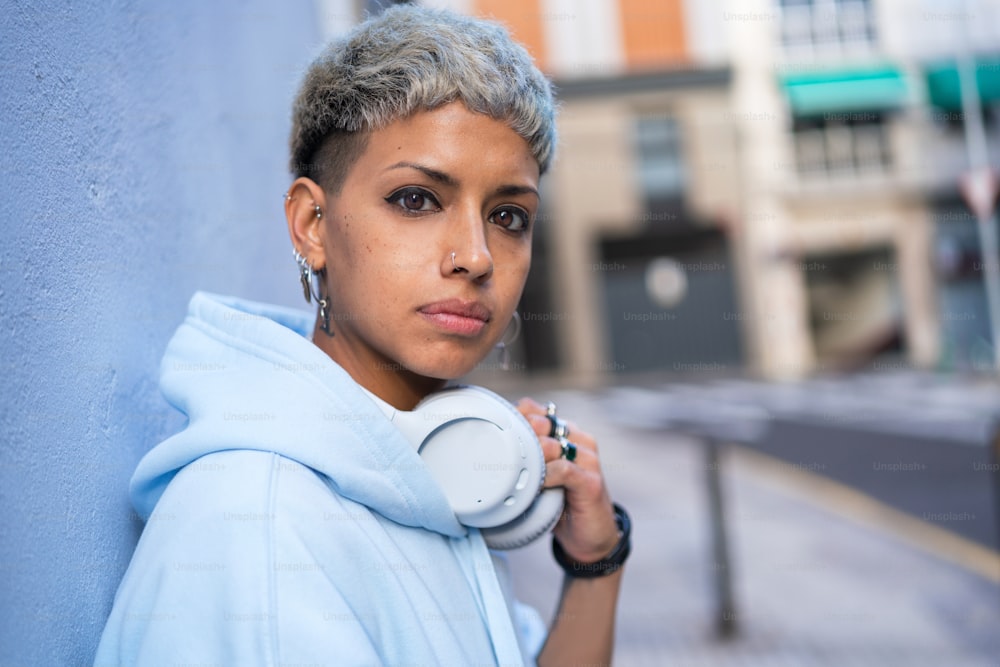 Young beautiful woman with short haircut posing with white headphones, looking at the camera. Real people emotions. Hobby. Dj. Lifestyle concept. City walk.