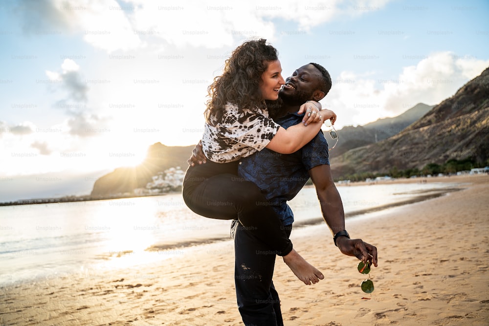 Beautiful multiracial happy young couple laughing, having fun together on the beach. Multi ethnic love concept. Smiling woman and handsome man. Summer time. Traveler. Real people emotions.