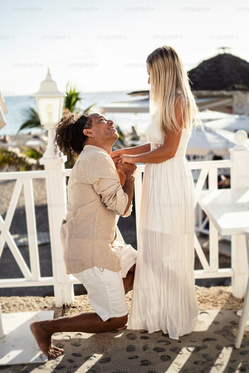 Romantic scene of a happy man making proposal to his beautiful woman on the beach. Real people lifestyle. Love. Multiethnic couple.