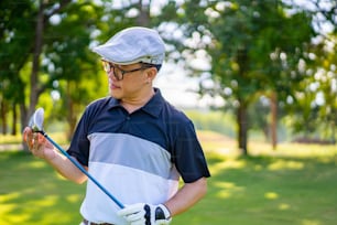Portrait of Smiling Asian man holding golf club standing on golf course fairway in sunny day. Healthy male golfer enjoy outdoor lifestyle activity sport golfing at country club on summer vacation