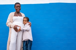 Niño pequeño haciendo símbolo de corazón con mamá en su vientre de embarazada, abrazándola, sonriendo. Familia africana. Estilo de vida de personas reales. Mucho espacio de copia.