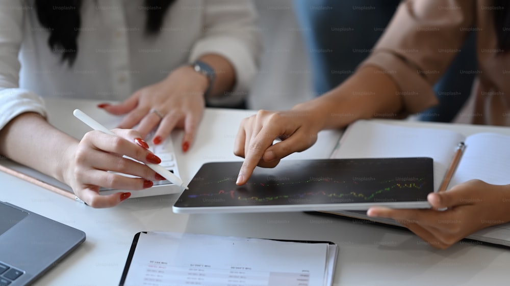 Immagine ritagliata di due donne d'affari che analizzano insieme il grafico finanziario sulla tavoletta digitale.