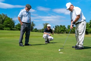 Group of Asian people businessman and senior CEO golfing near the hole on golf fairway together at country club. Healthy elderly man golfer enjoy outdoor golf sport and leisure activity with friends.