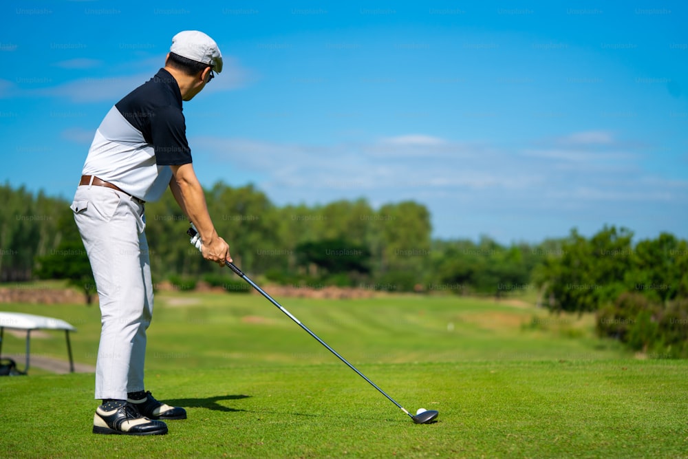 Confidence Asian man golfer holding golf club hitting golf ball on the green at golf course in sunny day. Healthy male enjoy outdoor lifestyle activity sport golfing at country club on summer vacation