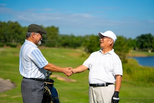 Asian people businessman senior CEO shaking hand after finish talking business project and golfing together at golf course. Elderly male friends golfer enjoy outdoor sport golfing together at country club.