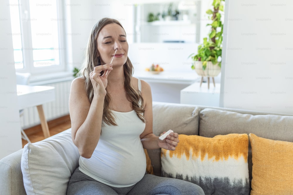 Une femme enceinte effectue un auto-écouvillonnage à domicile pour les tests de dépistage de la COVID-19 à domicile avec un kit antigénique. Présentation d’un stick nasal pour vérifier l’infection par le coronavirus. Quarantaine, pandémie.