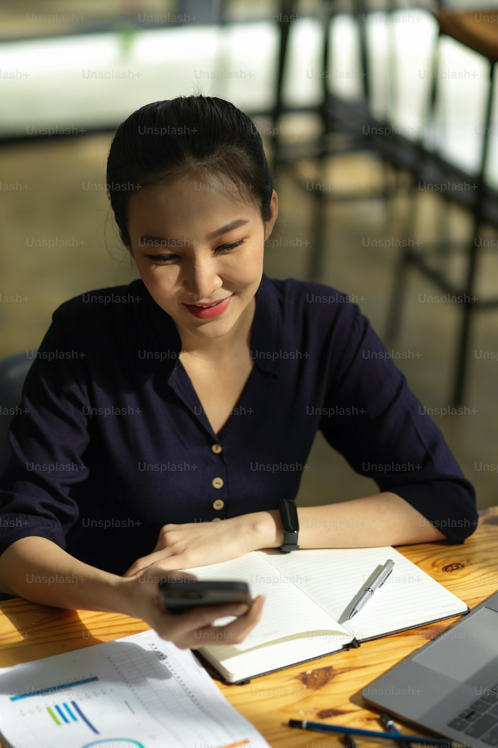 Ritratto di una bella donna asiatica che usa lo smartphone alla scrivania del suo ufficio. Chat femminile, messaggio, testo con i suoi amici.