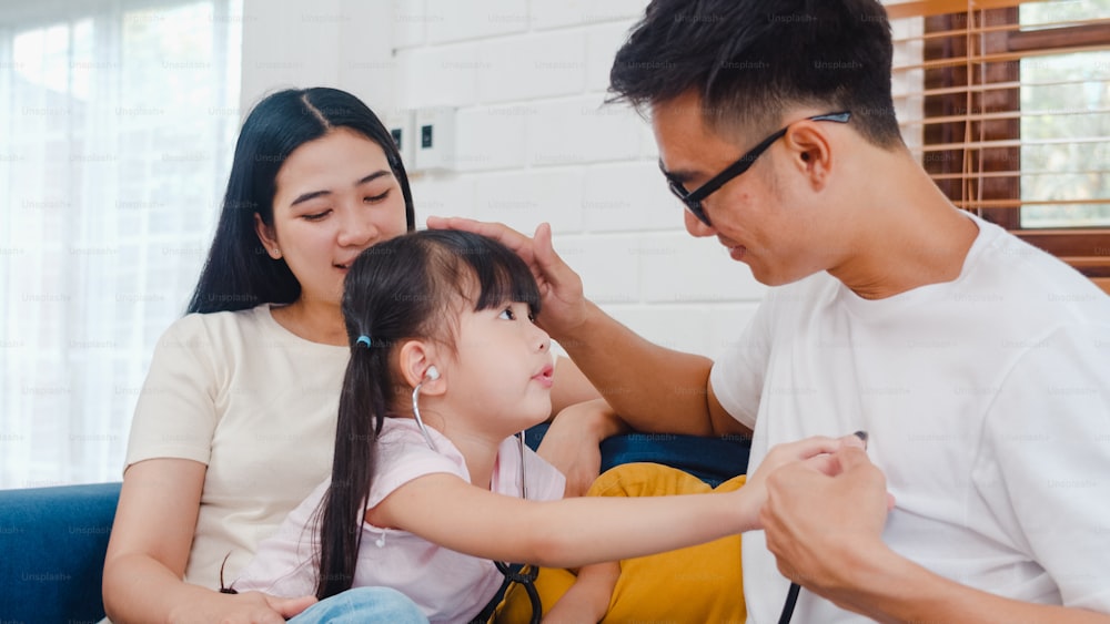 행복한 쾌활한 아시아 가족 아빠, 엄마, 딸은 집에서 소파에서 즐거운 시간을 보내는 의사로 재미있는 게임을 하고 있습니다.