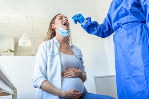 Physician wearing personal protective equipment performing a Coronavirus COVID-19 PCR test, pregnant woman nasal NP and oral OP swab sample specimen collection process, viral rt-PCR DNA procedure