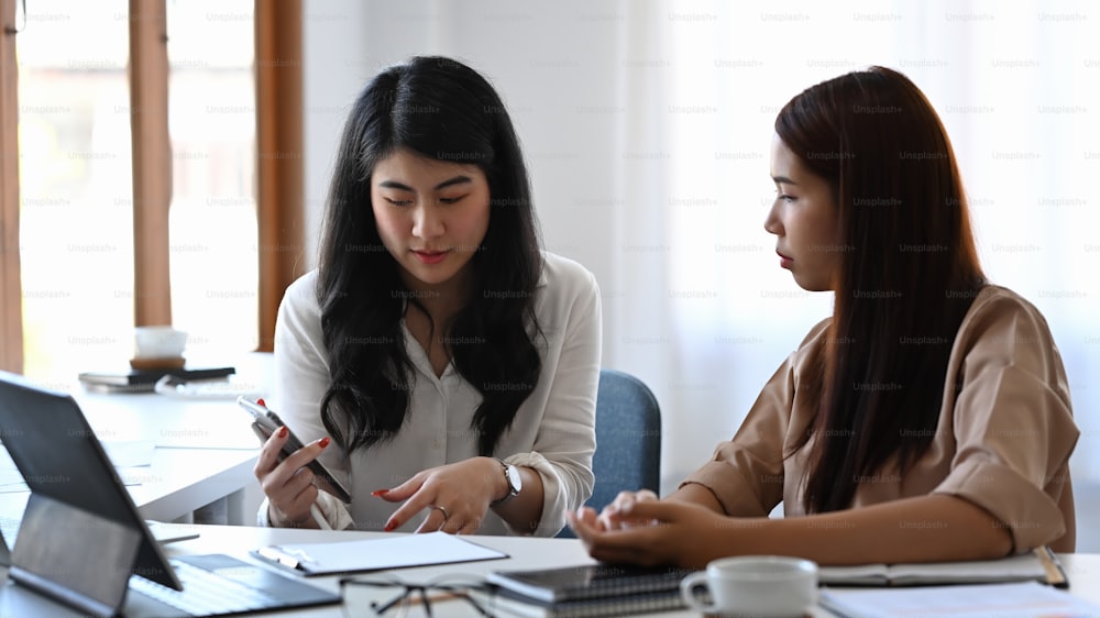 Empresária asiática compartilhando informações em seu smartphone para seu colega.