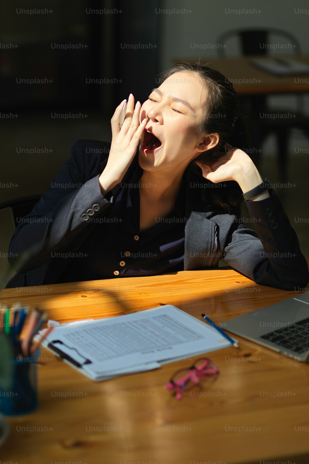 Schläfrige asiatische Geschäftsfrau gähnt an ihrem Schreibtisch. Schlafmangel, müde von überarbeitet, erschöpft und unruhig.