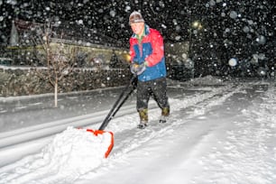 Älterer Mann mit einer Schaufel in der Hand räumt nach starkem Schneefall die Straße. Mann bei Saisonarbeit