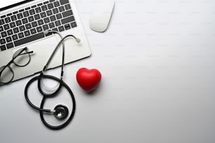 Top view laptop computer, stethoscope and red heart on white table. Cardiology and life insurance concept.