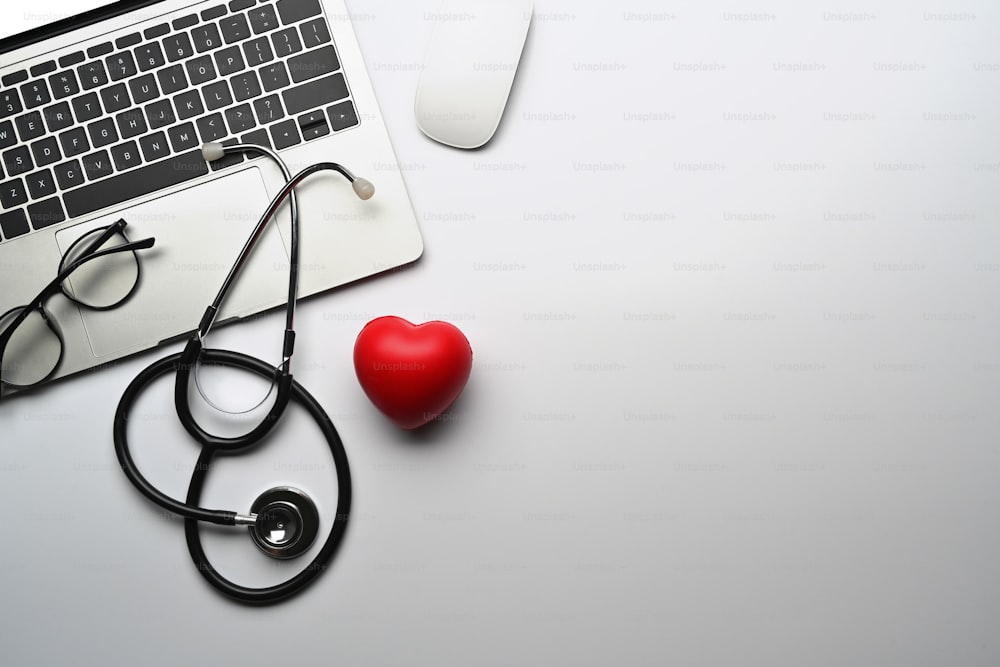 Vista superior computador portátil, estetoscópio e coração vermelho na mesa branca. Cardiologia e conceito de seguro de vida.
