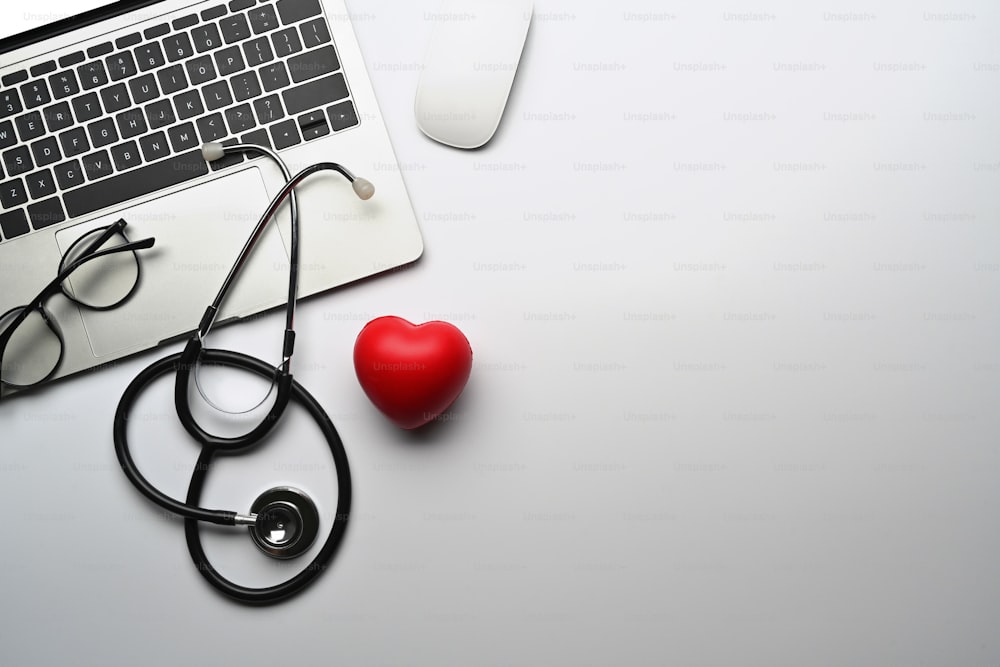 Top view laptop computer, stethoscope and red heart on white table. Cardiology and life insurance concept.