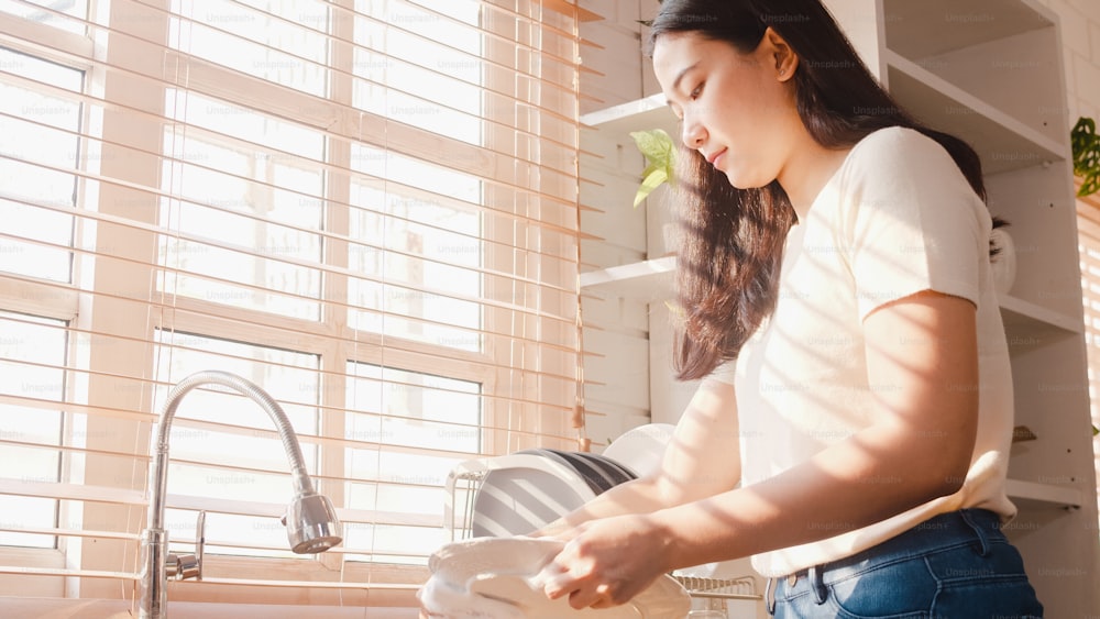 自宅の台所で掃除をしながら皿洗いをする魅力的なアジアの若い女性。