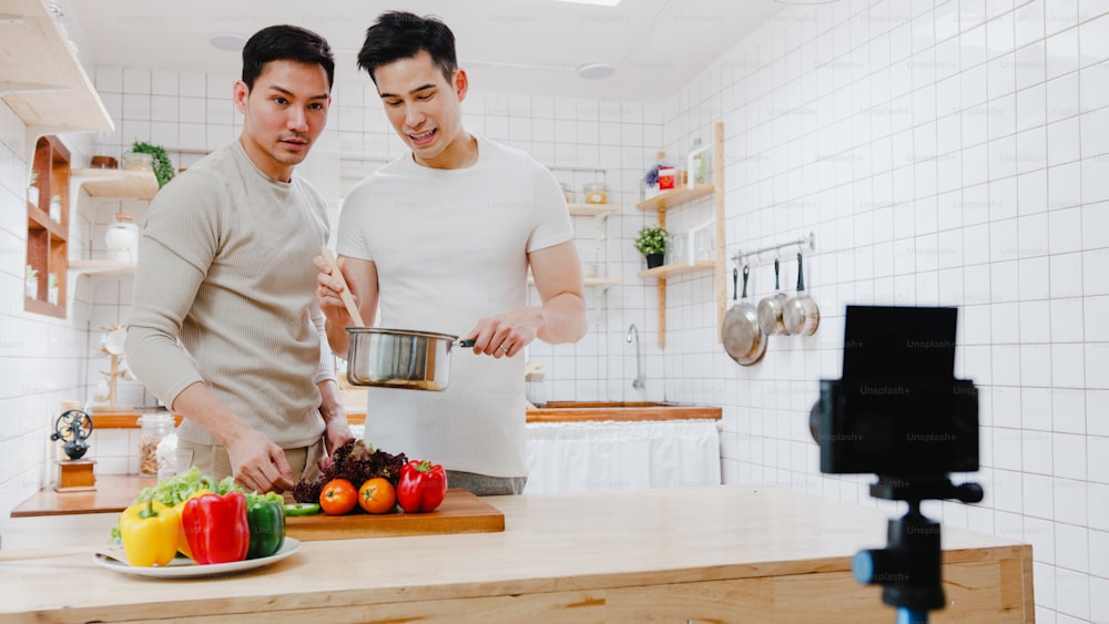 Pareja gay asiática, bloguera, vlogger e influencer en línea grabando contenido de video sobre comida saludable en la cocina de su casa.