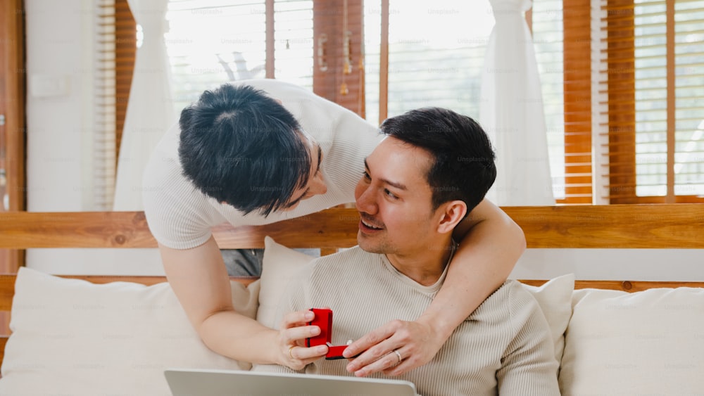Young Asia gay couple propose at modern home, LGBTQ men happy smiling have romantic time while proposing and marriage surprise wear wedding ring in living room at house.
