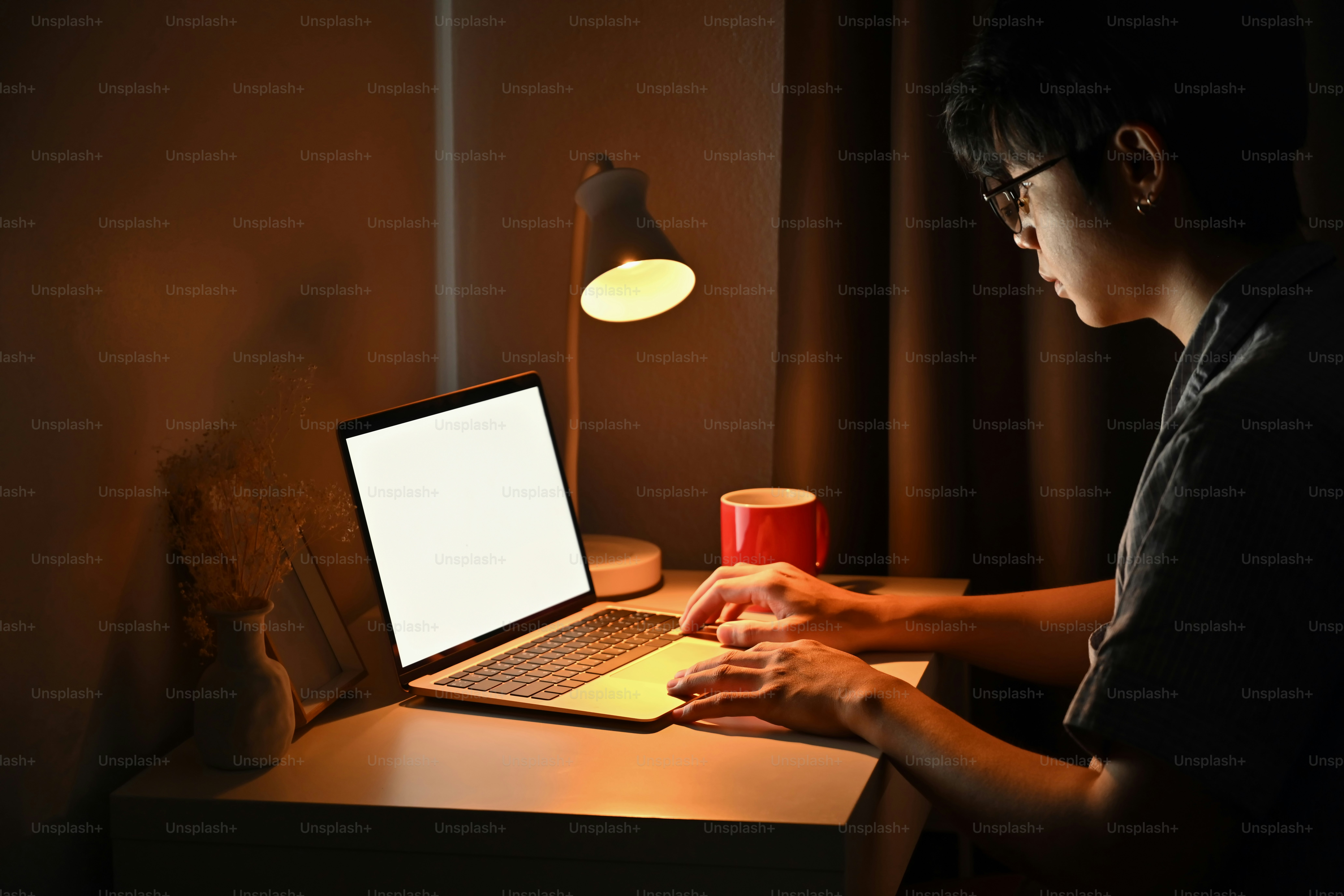 A young man working alone late at night under a desk lamp, focused and determined mood