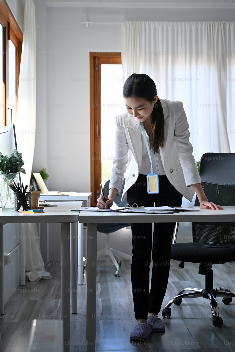 Full length portrait of businesswoman standing at her workplace and signing on business document.