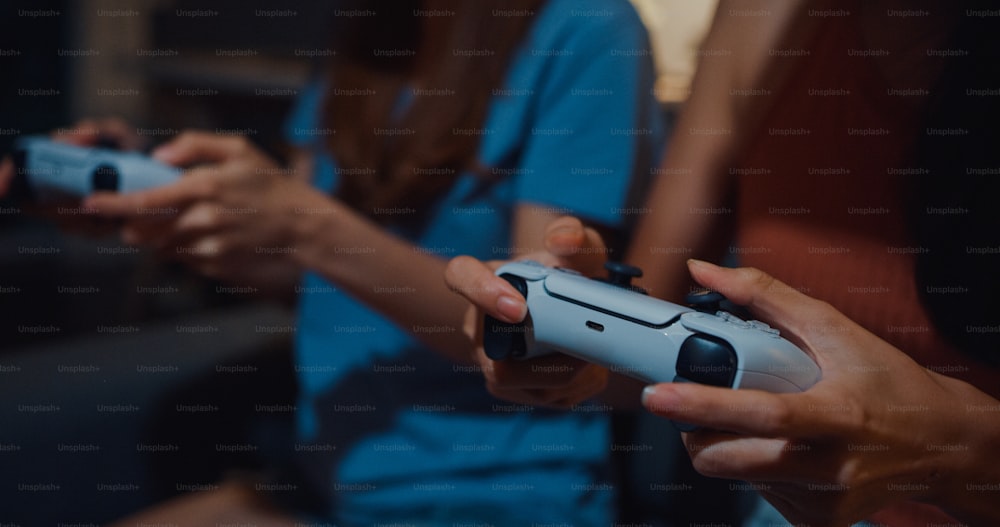 Enfoque de primer plano Asia pareja damas mano disfrutar de un momento feliz uso del gamepad del controlador jugando al sitio de videojuegos en la sala de estar del sofá en casa en la noche oscura.