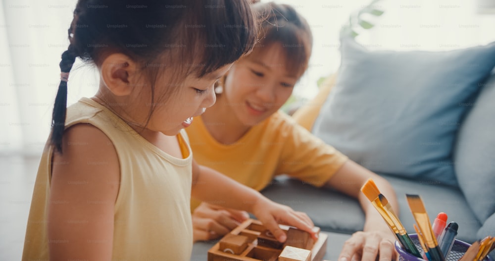 Happy Asia family mom teach girl play board game hobby with wooden box having fun relax on couch in living room at house. Spending time together, Social distance, Quarantine for coronavirus.